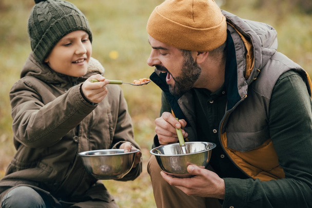 Son giving spoon with beans to father - Photo, Image