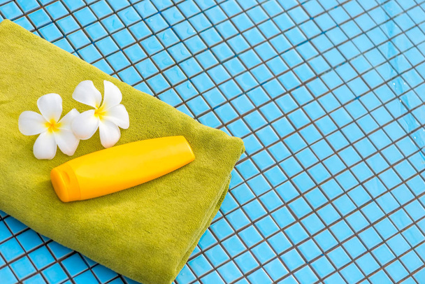 on a blue pool tile a green towel, a sun cream and beautiful flo - Foto, immagini