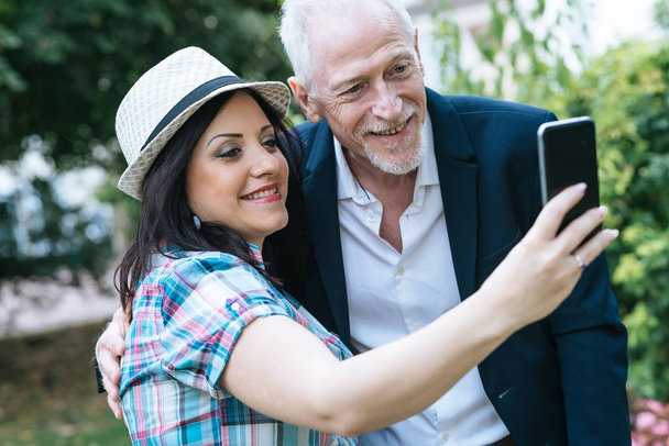 Mutlu genç kadın ve olgun adam selfie çekiyorlar. - Fotoğraf, Görsel