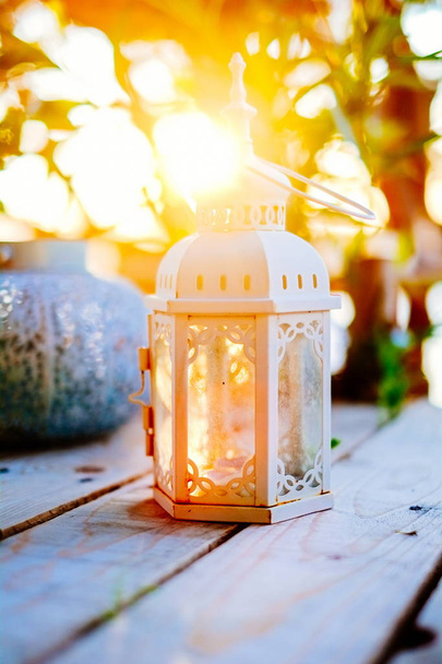 Lanterna decorativa bianca candela primo piano su tavolo di legno con bel tramonto sullo sfondo
 - Foto, immagini