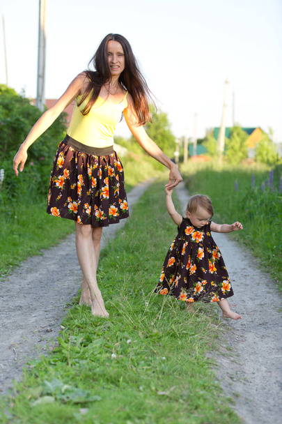 Mutter und Baby gehen barfuß auf einer Landstraße im gleichen Kleid - Foto, Bild