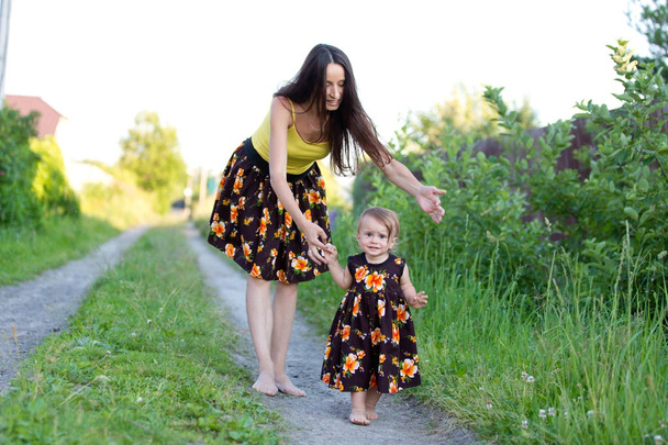 Mom and baby girl walking barefoot on a country road in the same dress - Photo, Image