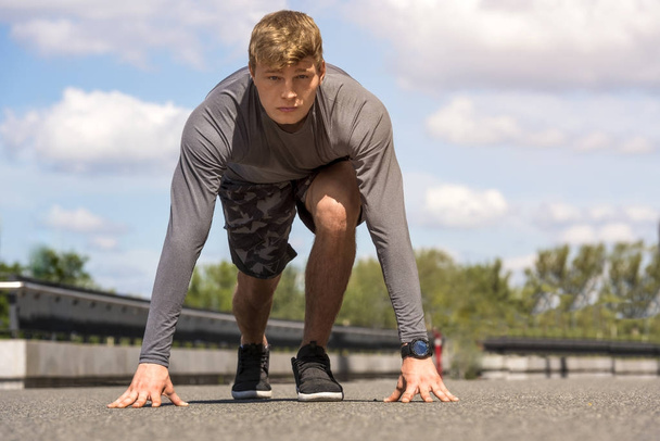 Junger Mann startet Lauf, draußen bei sonnigem Tag in Sportbekleidung in grau - Foto, Bild