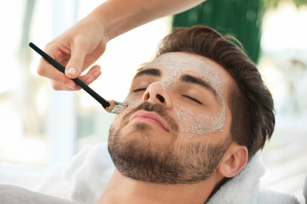 Beautician applying scrub onto young man's face in spa salon - Фото, зображення