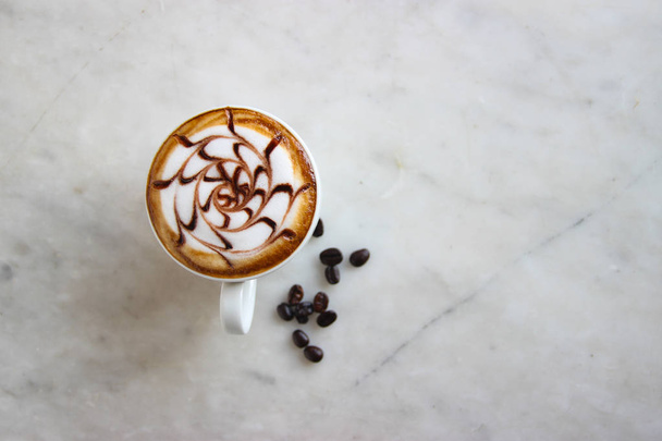Vista superior, cerrado latte caramelo caliente con el arte del patrón de vapor de leche, decorar con frijoles y hojas verdes
. - Foto, Imagen