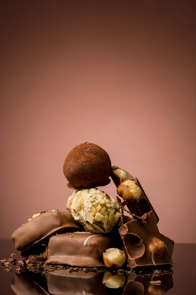 Pile of broken chocolate on table against brown studio background - Fotoğraf, Görsel