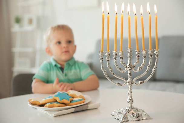 Cute boy sitting at table with nine-branched menorah and festive cookies - Photo, Image