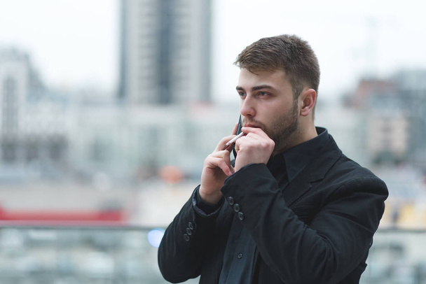 Biznesmen pali papierosa i mówi przez telefon na tle krajobrazu miasta. - Zdjęcie, obraz