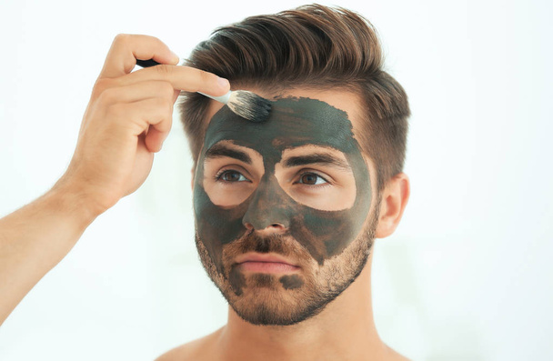 Young man applying cosmetic mask on his face in bathroom - Φωτογραφία, εικόνα