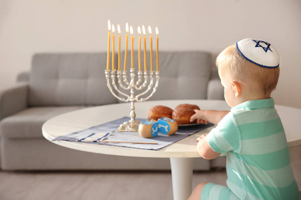 Cute boy sitting near nine-branched menorah on table at home - Photo, Image