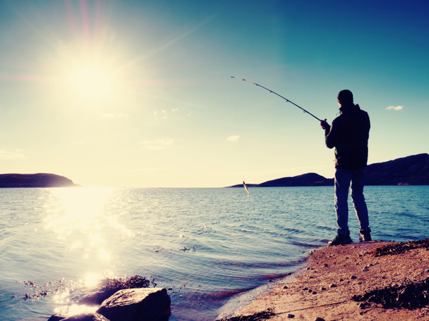 Рибалка перевіряє рибальську лінію і штовхає приманку на стрижень. Силует рибалки на заході сонця
  - Фото, зображення