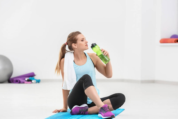 Sporty young woman with bottle of water in gym - Foto, afbeelding