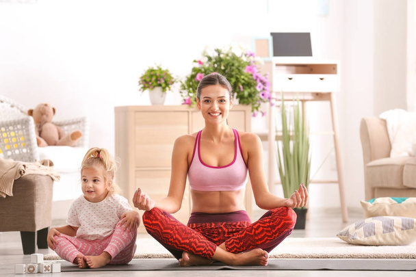 Hermosa joven con hija pequeña practicando yoga en casa
 - Foto, Imagen