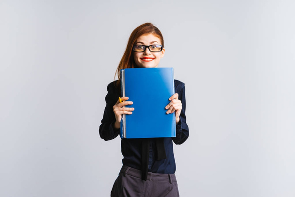 cute girl with red lips in glasses holds a blue folder and looks into the camera, isolated on a white background - Fotoğraf, Görsel