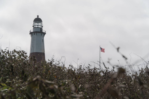 モントーク ポイント灯台とアメリカ国旗海風風は、秋の日に背の高いスタンドします。海上輸送のロングアイランドの州立公園の場所歴史博物館末ビーコン回転灯インジケーター - 写真・画像