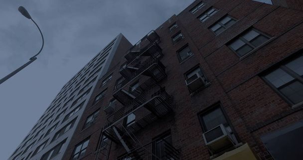 Exterior photo NYC style apartment building above store front awnings at night. Vertical look up to windows and fire escape on facade - Fotó, kép