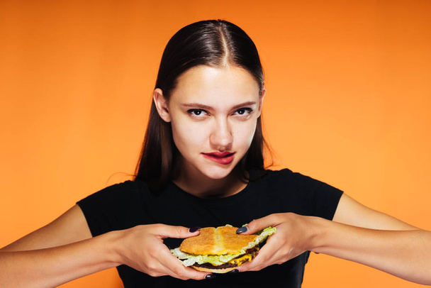 sexy girl in a black T-shirt is about to eat an appetizing burger and looks at the camera - Photo, image