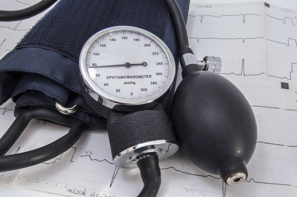 Esfigmomanómetro aneroide con indicadores fisiológicos normales de presión arterial, bombilla, válvula de aire, manguito y tubo flexible negro se encuentra en el electrocardiograma de papel (ECG o ECG
) - Foto, Imagen