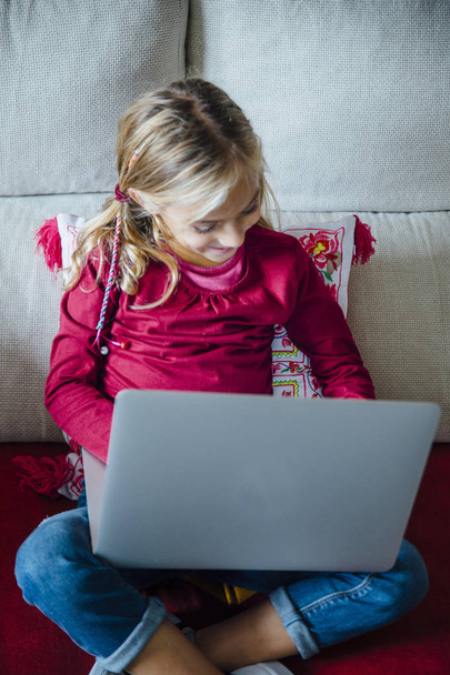 Счастливая маленькая девочка лежит на диване с ноутбуком в гостиной
 - Фото, изображение