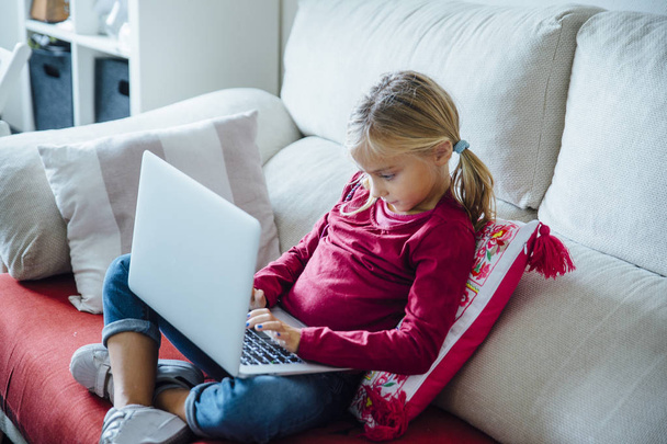 Щаслива маленька дівчинка лежить на дивані з ноутбуком в живому р
 - Фото, зображення