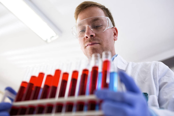 Young chemist in the laboratory holding tubes  - Φωτογραφία, εικόνα