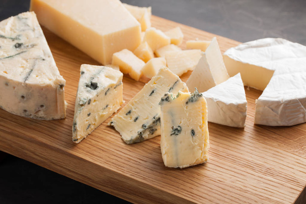 Degustación de plato de queso en un plato de madera. Comida para el vino y romántica, delicatessen queso en una mesa de piedra oscura
 - Foto, Imagen
