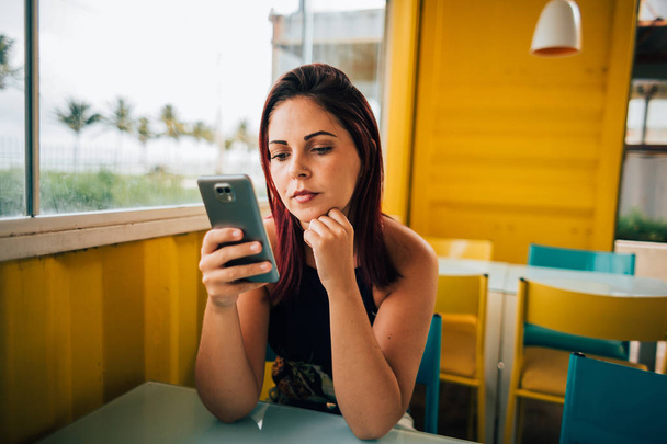 Portrait of beautiful young woman sitting in cafe and looking at mobile phone - Foto, Imagem