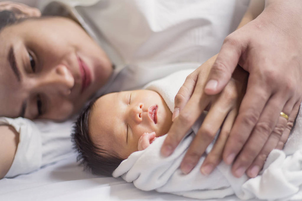 Young asian parents lying on bed and holding newborn baby - Фото, зображення