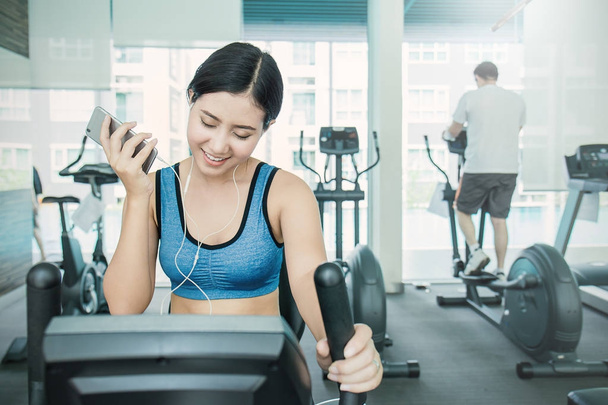 Beautiful asian woman listening music from smartphone at gym - Photo, image