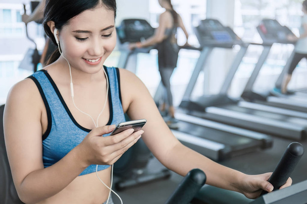 Beautiful asian woman listening music from smartphone at gym - Foto, afbeelding