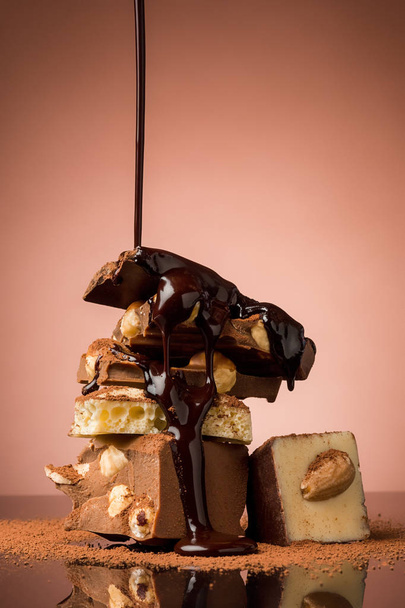 Pile of broken chocolate on table against brown studio background and hot chocolate spray - Foto, Imagem