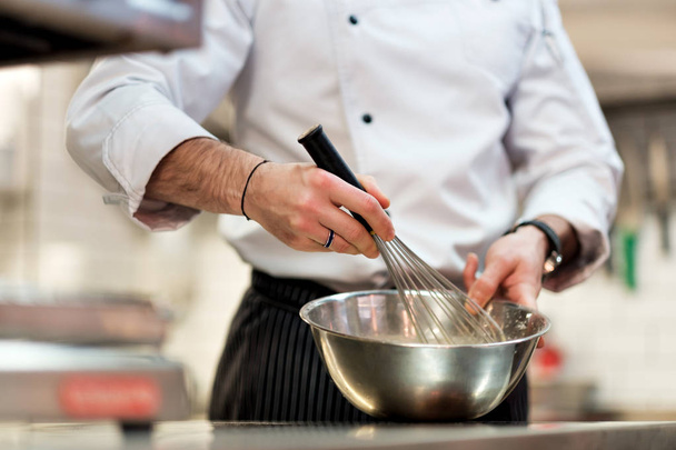 Chef in hotel or restaurant kitchen cooking, only hands. He is whisking ingredients. - Foto, Bild