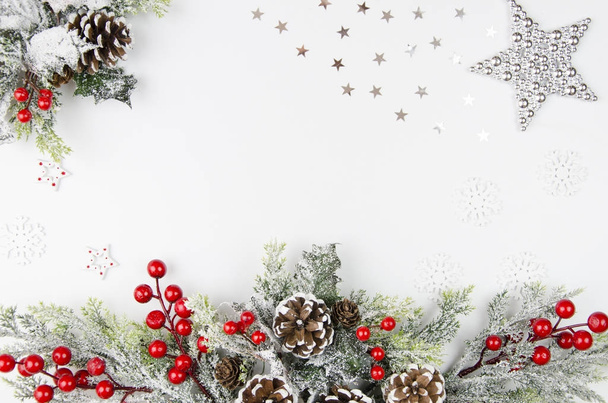 Kreativer Rahmen aus Weihnachtsdeko, Silberstern, Tannenzweigen, Tannenzapfen und roten Beeren auf weißem Tisch. flaches Layout und Zusammensetzung von oben. Attrappe - Foto, Bild