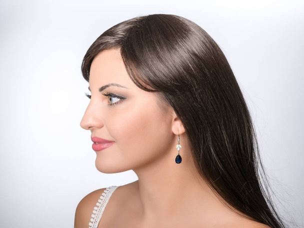 Belle fille avec des cheveux bruns portant des boucles d'oreilles goutte, pierre gemme bleue, bijoux
 - Photo, image
