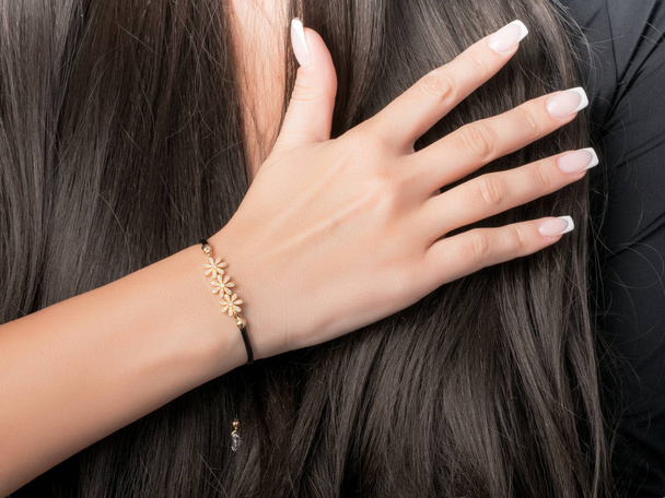 Gold bracelet on a hand with French manicure, bracelet with flower, black chain - Фото, зображення