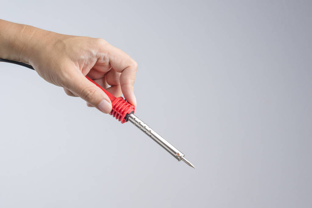 Mão segurando ferro de solda com uma alça vermelha para aquecimento para derreter a solda em equipamento eletrônico sobre fundo branco
 - Foto, Imagem