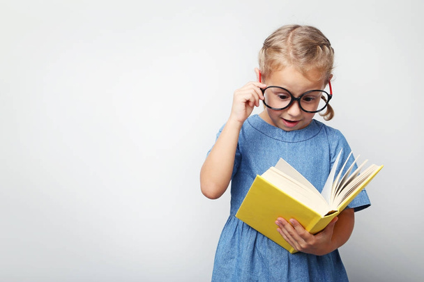 Portrait of little girl with glasses and book on grey background - Valokuva, kuva