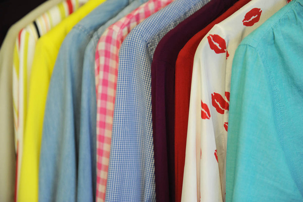 Υφή φόντου από μια σειρά από χρωματισμένα πουκάμισα και μπλούζες σε μια κρεμάστρα - Φωτογραφία, εικόνα