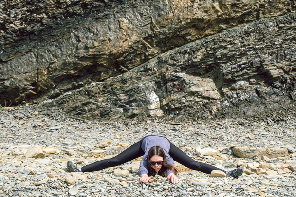Girl practicing yoga on the rocks stands on a stone - Foto, afbeelding