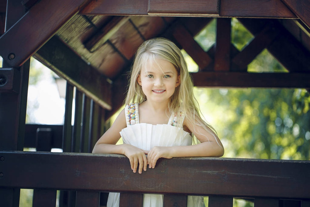 Маленькая девочка на детской площадке. деревянный дом. солнечный день. Лето
 - Фото, изображение