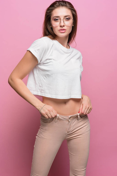 Pretty young sexy fashion sensual woman posing on pink background dressed in hipster style jeans - Fotografie, Obrázek