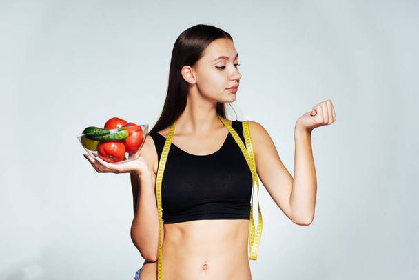 young sporty girl watches her figure, smiles, holds a glass plate with useful vegetables and fruits in her hands - Photo, image