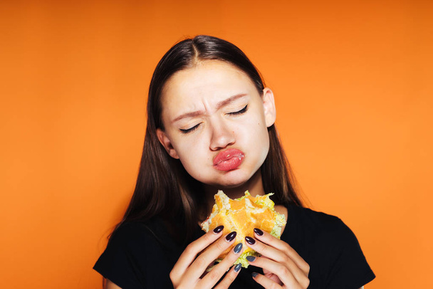 young beautiful happy girl wants to lose weight, but eagerly eats a harmful calorie burger - Photo, image