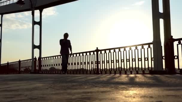 Un jeune homme marche sur un pont avec un smartphone à portée de main au coucher du soleil au ralenti
 - Séquence, vidéo