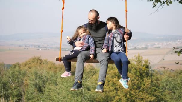 Papa swingen met dochters op een schommel onder een boom. - Video