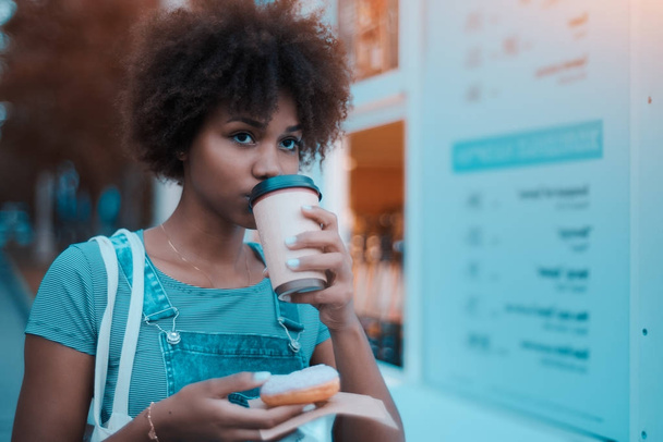 Black young female with donut and coffee outdoors - Foto, Imagen