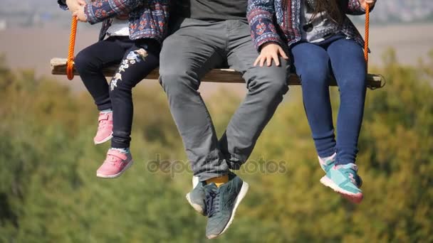 Ноги отца, качающегося с дочерьми на качелях под деревом. Крупный план
 - Кадры, видео