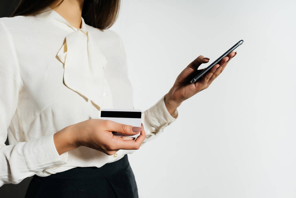 young successful modern girl holding a bank card and smartphone in her hand - Photo, Image