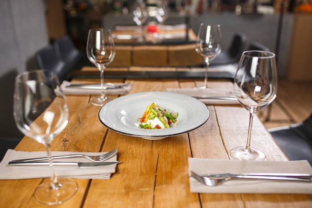 Een houten tafel in het restaurant geserveerd met bril in het midden, is een gerecht met vegetarische salade mozzarella kaas en groenten - Foto, afbeelding