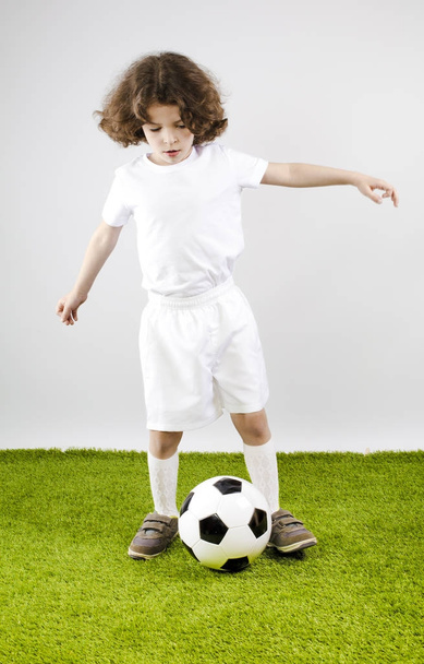 Young football player playing soccer on the grass. Gray background. - 写真・画像